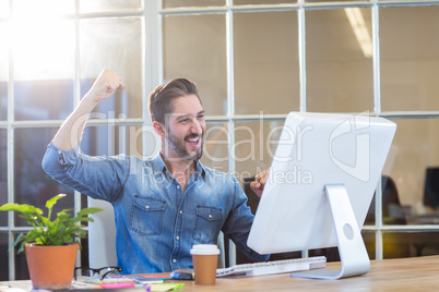 Casual businessman cheering in front of his computer