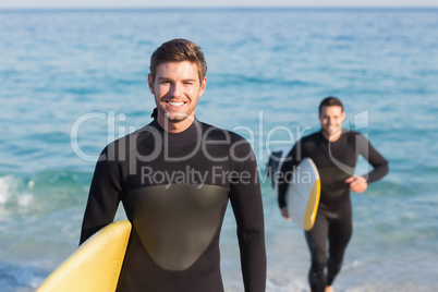 Two men in wetsuits with a surfboard on a sunny day