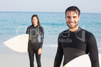 happy couple in wetsuits with surfboard on a sunny day