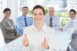 Smiling businesswoman giving thumbs up with her team behind