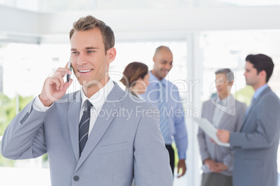 Businessman having phone call while his colleagues discussing