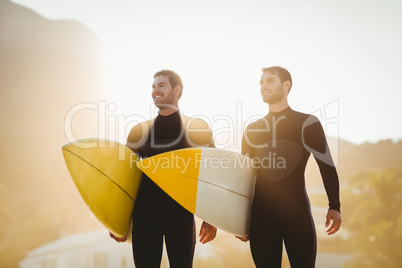 Two men in wetsuits with a surfboard on a sunny day