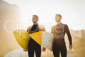 Two men in wetsuits with a surfboard on a sunny day