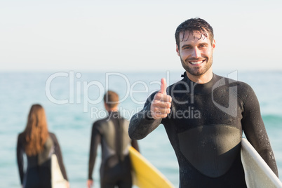 Group of friends on wetsuits with a surfboard on a sunny day