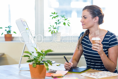 Smiling casual businesswoman working on digitizer and holding co