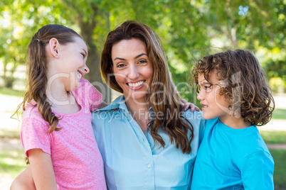 mother and children smiling and kissing in a park