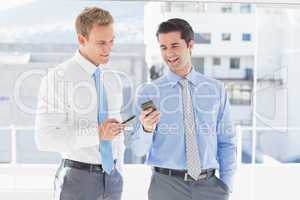 Two businessmen talking to each other and texting