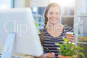 Smiling casual businesswoman working on digitizer and holding co