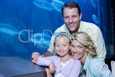 Happy family looking at camera beside the fish tank