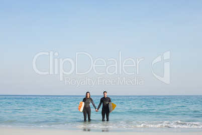 happy couple in wetsuits with surfboard on a sunny day