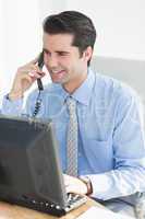 Businessman having phone call while using his laptop