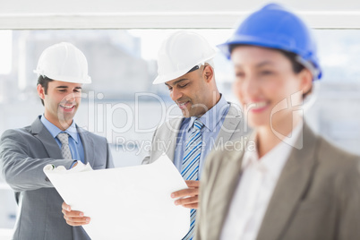 Businessmen and a woman with hard hats and holding blueprint