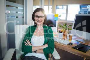 Smiling brunette sitting at her desk arms crossed