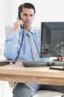 Businessman having phone call while using his computer