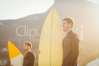 Two men in wetsuits with a surfboard on a sunny day