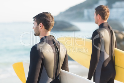 Two men in wetsuits with a surfboard on a sunny day