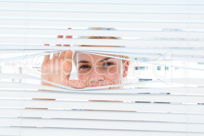 Curious blonde woman looking through venetian blind