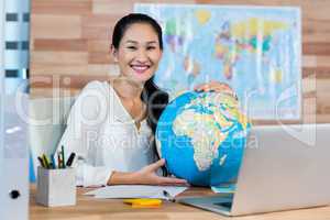 Pretty travel agent holding globe and smiling at camera