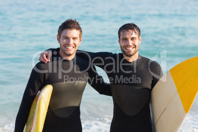 Two men in wetsuits with a surfboard on a sunny day