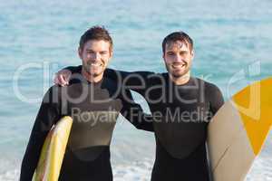 Two men in wetsuits with a surfboard on a sunny day