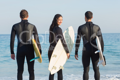 Group of friends on wetsuits with a surfboard on a sunny day