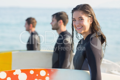 Group of friends on wetsuits with a surfboard on a sunny day