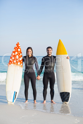 happy couple in wetsuits with surfboard on a sunny day