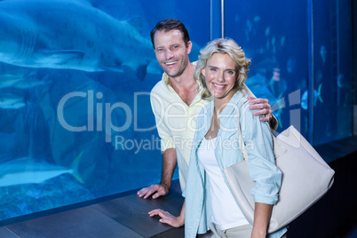 Happy couple looking at camera beside the fish tank