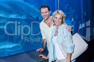 Happy couple looking at camera beside the fish tank