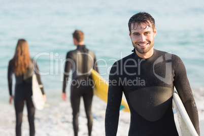Group of friends on wetsuits with a surfboard on a sunny day Group of friends on wetsuits with a surfboard on a sunny day