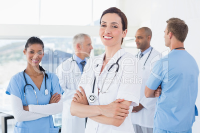 Confident female doctor smiling at camera with her team behind