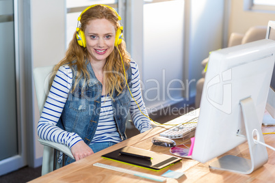 Smiling businesswoman sitting at her desk and listening music