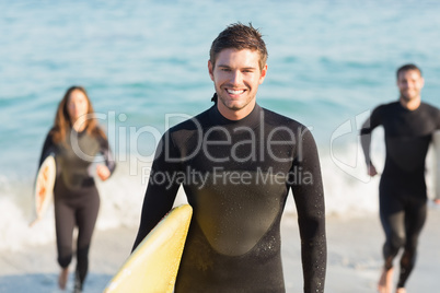 Group of friends on wetsuits with a surfboard on a sunny day