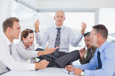 Businessman relaxing on the desk with upset colleagues around