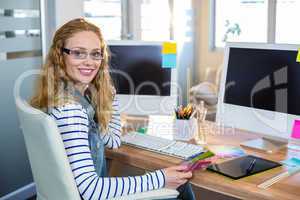 Smiling designer sitting at her desk and looking at colour swatc