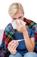Sick blonde woman blowing her nose and checking the thermometer