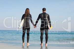 happy couple in wetsuits with surfboard on a sunny day