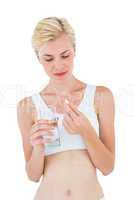 Fit blonde woman looking at pill and glass of water
