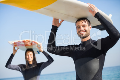 happy couple in wetsuits with surfboard on a sunny day