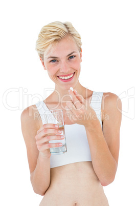 Smiling blonde woman holding pill and looking at camera