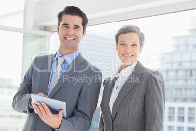 Business colleagues smiling at camera and holding tablet