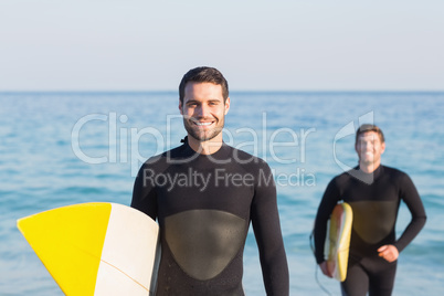 Two men in wetsuits with a surfboard on a sunny day