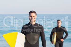 Two men in wetsuits with a surfboard on a sunny day