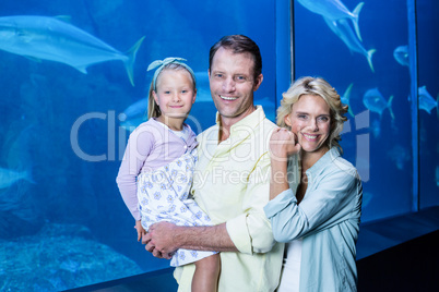 Happy family looking at camera beside the fish tank