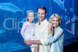 Happy family looking at camera beside the fish tank