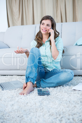 Woman calling while calculating bills with laptop
