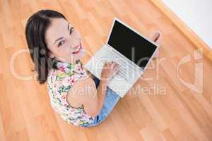 Pretty brunette looking at camera and using laptop on the floor