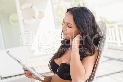 Pretty brunette sitting on a chair and reading magazine