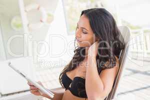 Pretty brunette sitting on a chair and reading magazine