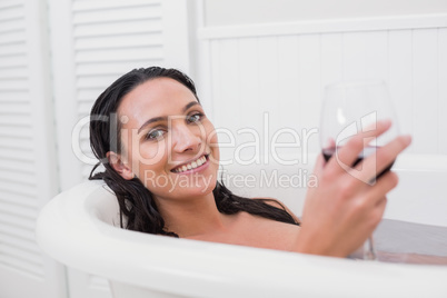Pretty brunette taking a bath with glass of wine